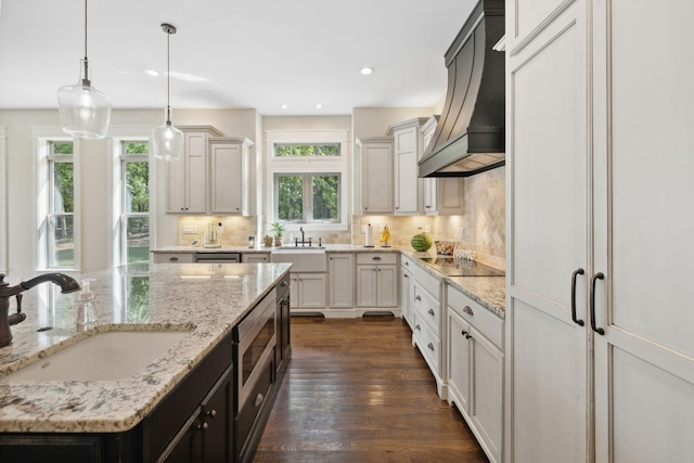 kitchen with sink, light stone counters, decorative light fixtures, white cabinets, and custom range hood