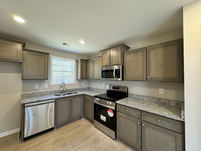 kitchen with appliances with stainless steel finishes, light hardwood / wood-style flooring, light stone counters, and sink