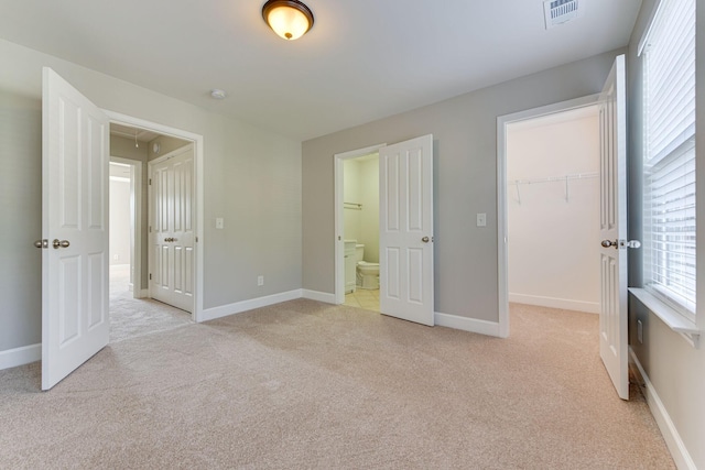 unfurnished bedroom with ensuite bathroom, a spacious closet, light carpet, and a closet