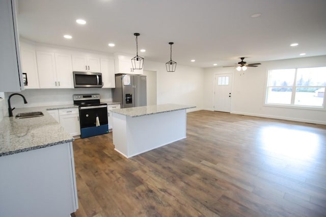 kitchen with white cabinets, sink, appliances with stainless steel finishes, decorative light fixtures, and a kitchen island