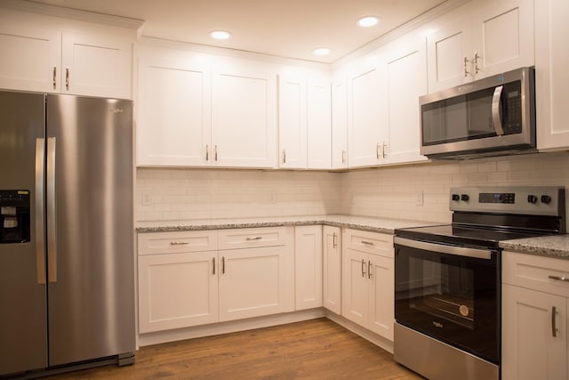 kitchen with backsplash, white cabinets, light stone counters, wood-type flooring, and stainless steel appliances