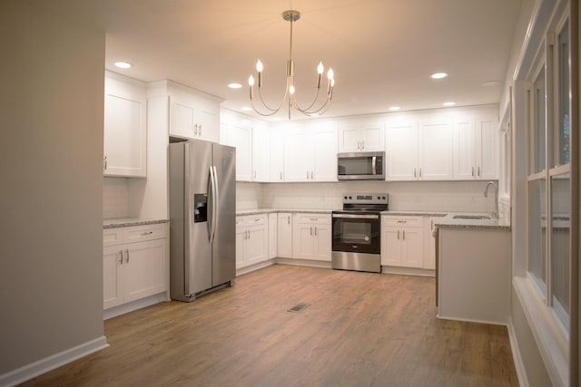 kitchen featuring hardwood / wood-style floors, sink, hanging light fixtures, white cabinetry, and stainless steel appliances