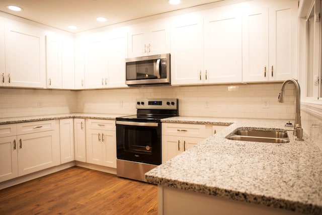 kitchen featuring light stone countertops, white cabinetry, sink, hardwood / wood-style floors, and appliances with stainless steel finishes