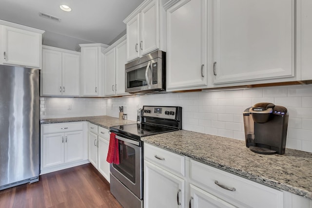 kitchen with light stone countertops, appliances with stainless steel finishes, decorative backsplash, white cabinets, and dark hardwood / wood-style floors