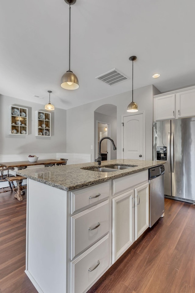 kitchen featuring appliances with stainless steel finishes, dark hardwood / wood-style flooring, pendant lighting, a center island with sink, and white cabinetry