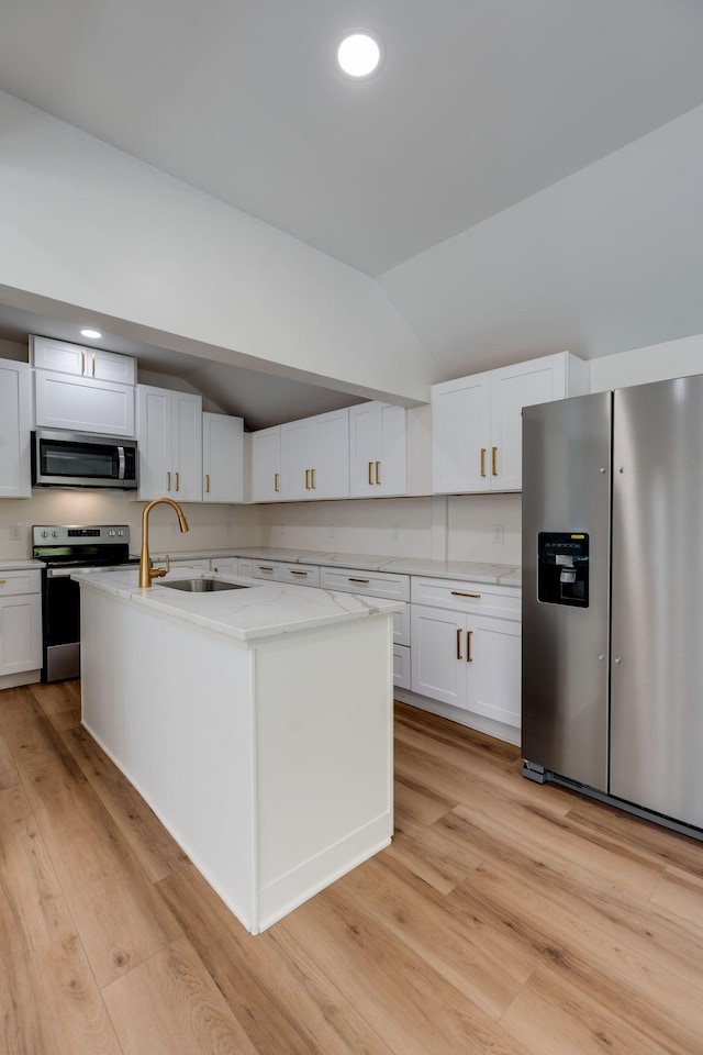 kitchen with vaulted ceiling, a center island with sink, white cabinetry, light stone countertops, and appliances with stainless steel finishes