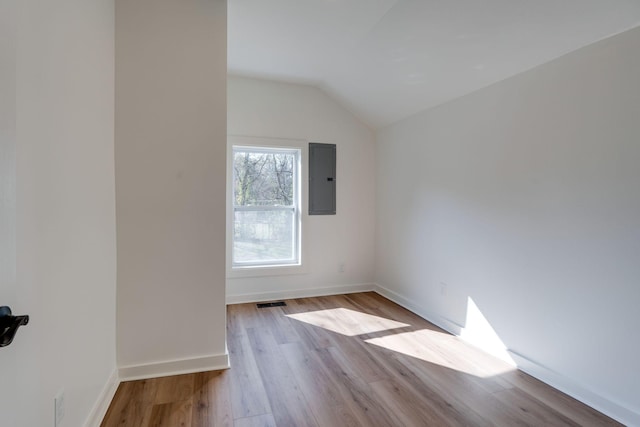 spare room with lofted ceiling, light wood-type flooring, and electric panel