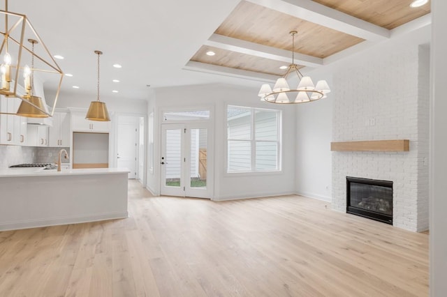 unfurnished living room with an inviting chandelier, a brick fireplace, beamed ceiling, light hardwood / wood-style floors, and wood ceiling