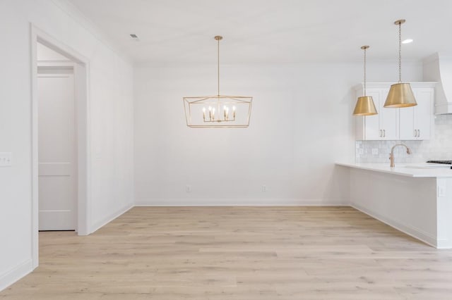 unfurnished dining area featuring crown molding, sink, light hardwood / wood-style floors, and an inviting chandelier