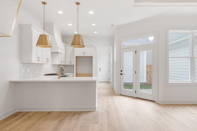 kitchen with light wood-type flooring, backsplash, custom range hood, pendant lighting, and white cabinets