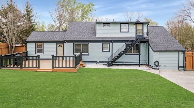 rear view of property featuring roof with shingles, stairway, a lawn, and fence