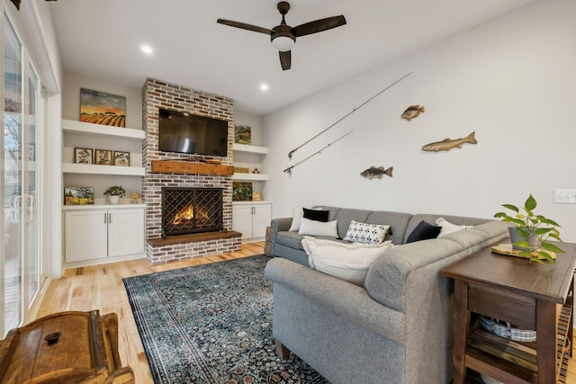 living room with ceiling fan, light hardwood / wood-style flooring, built in features, and a brick fireplace