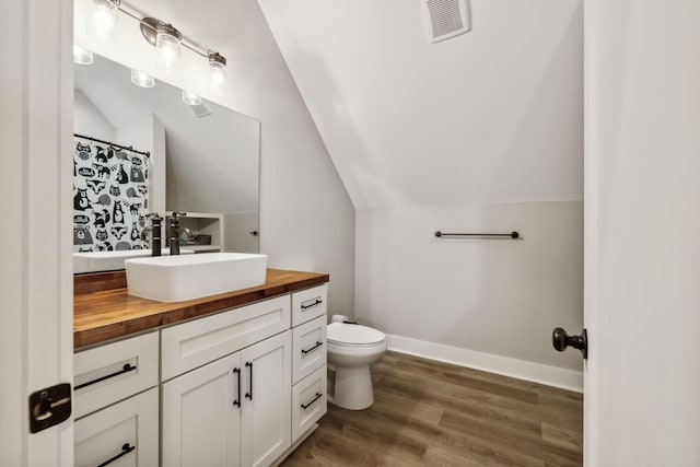 bathroom featuring hardwood / wood-style flooring, vanity, toilet, and vaulted ceiling