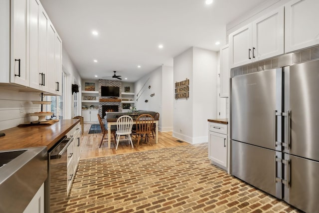 kitchen with white cabinets, stainless steel appliances, ceiling fan, and a fireplace