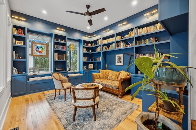 sitting room featuring built in shelves, ceiling fan, and light wood-type flooring