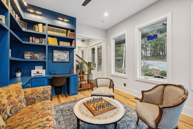 sitting room with built in shelves, ceiling fan, and light wood-type flooring