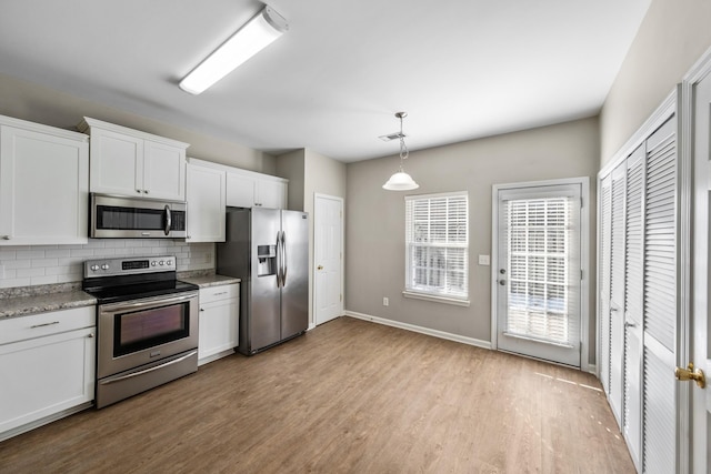 kitchen with appliances with stainless steel finishes, hanging light fixtures, decorative backsplash, and white cabinetry