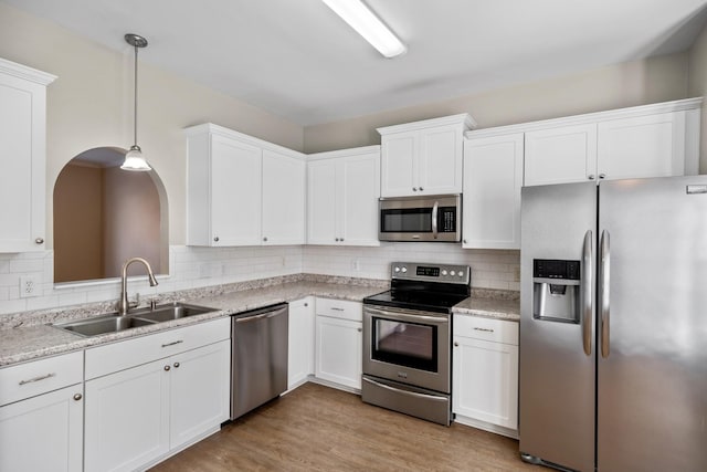 kitchen featuring stainless steel appliances, light wood-type flooring, sink, white cabinetry, and decorative light fixtures