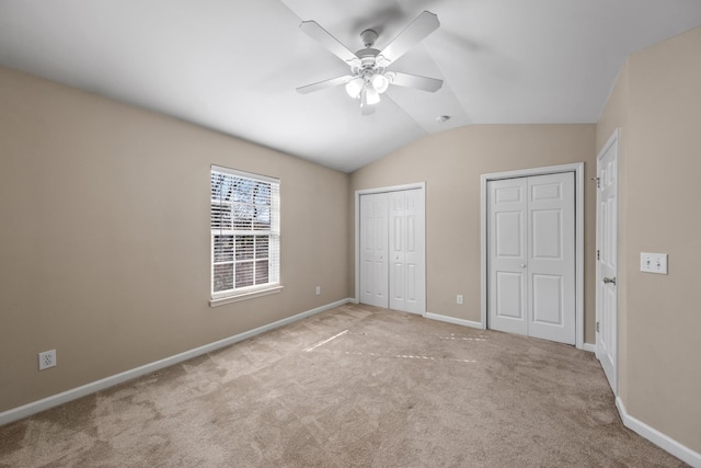 unfurnished bedroom with vaulted ceiling, two closets, ceiling fan, and light carpet