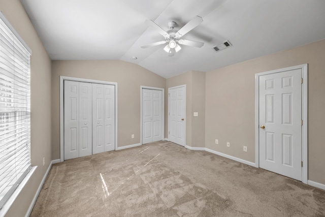 unfurnished bedroom featuring lofted ceiling, light carpet, ceiling fan, and multiple closets