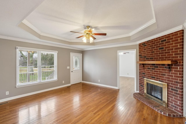 unfurnished living room featuring ceiling fan, a raised ceiling, crown molding, a fireplace, and hardwood / wood-style flooring