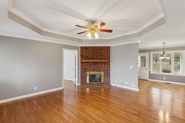 unfurnished living room featuring a raised ceiling, crown molding, a fireplace, ceiling fan with notable chandelier, and hardwood / wood-style flooring