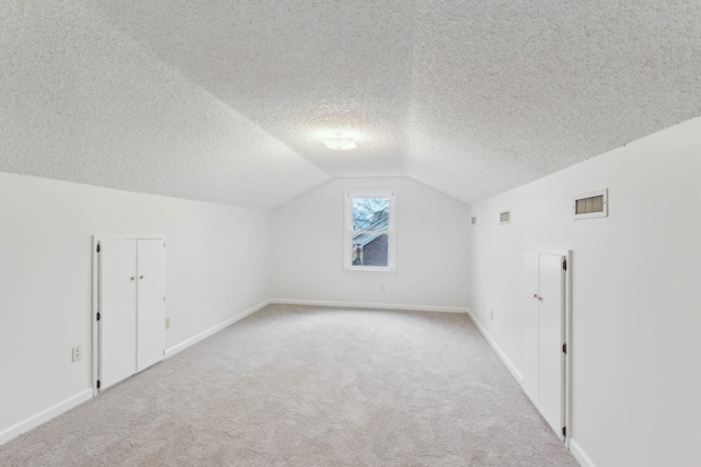 additional living space featuring a textured ceiling, light colored carpet, and vaulted ceiling