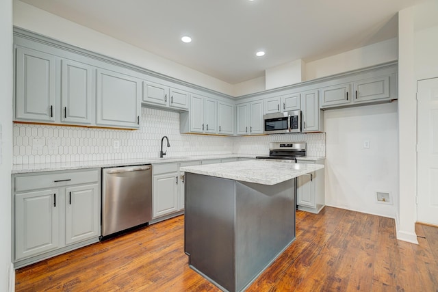 kitchen with sink, appliances with stainless steel finishes, light stone counters, a kitchen island, and dark hardwood / wood-style flooring