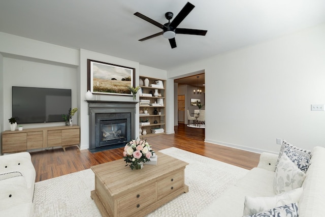 living room with hardwood / wood-style floors, ceiling fan with notable chandelier, and built in features