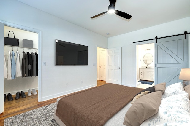 bedroom with ensuite bathroom, wood-type flooring, a closet, ceiling fan, and a barn door