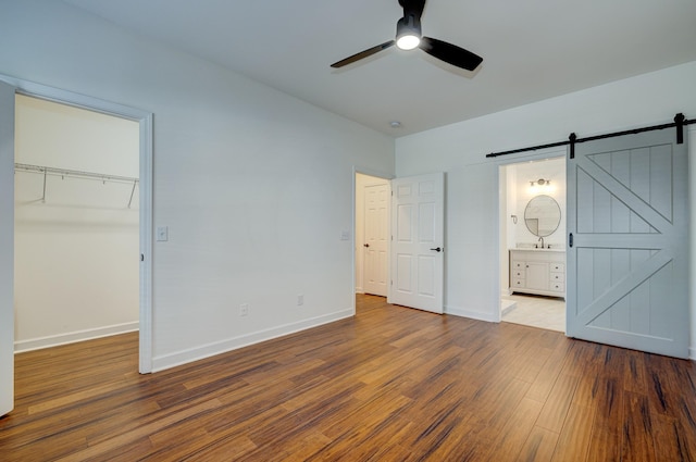 unfurnished bedroom with ensuite bath, hardwood / wood-style flooring, ceiling fan, a barn door, and a closet