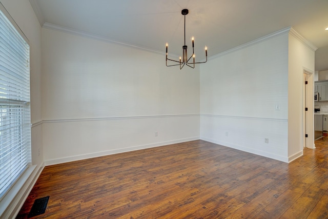 empty room with dark wood-type flooring, ornamental molding, and a notable chandelier