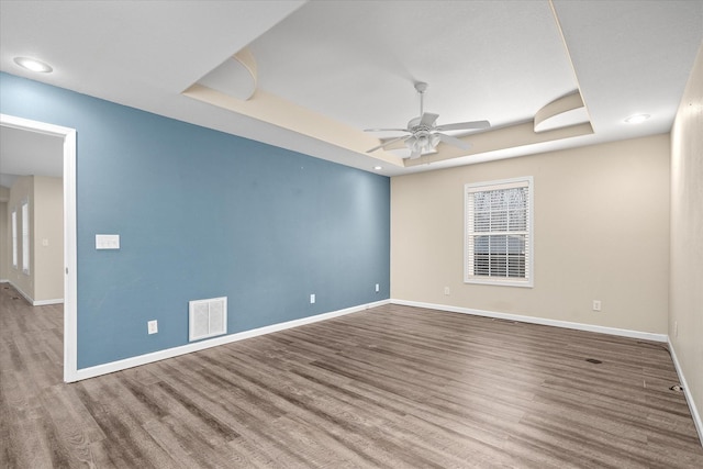 empty room featuring hardwood / wood-style flooring, ceiling fan, and a tray ceiling