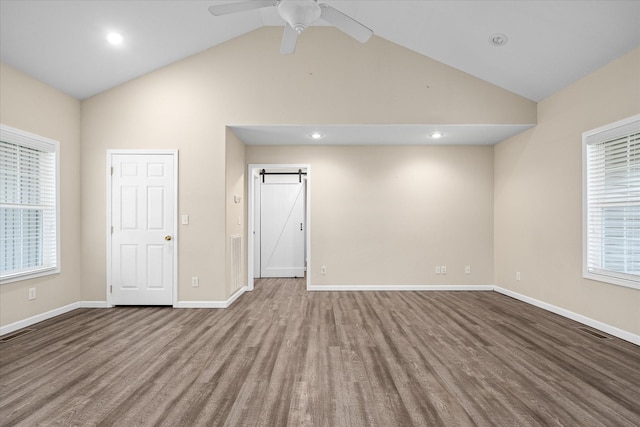 spare room featuring ceiling fan, a wealth of natural light, a barn door, lofted ceiling, and hardwood / wood-style flooring