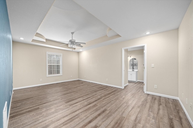 empty room featuring ceiling fan, a raised ceiling, and light wood-type flooring