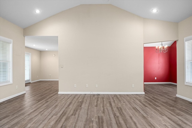 spare room featuring hardwood / wood-style floors, an inviting chandelier, and vaulted ceiling