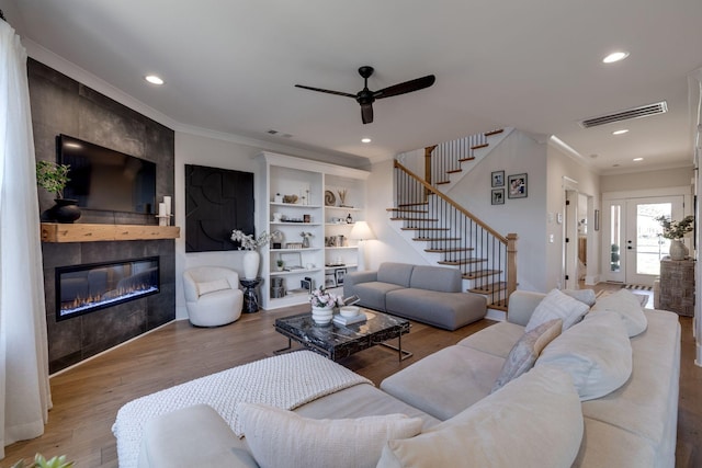 living room featuring a tiled fireplace, ceiling fan, light hardwood / wood-style flooring, and crown molding