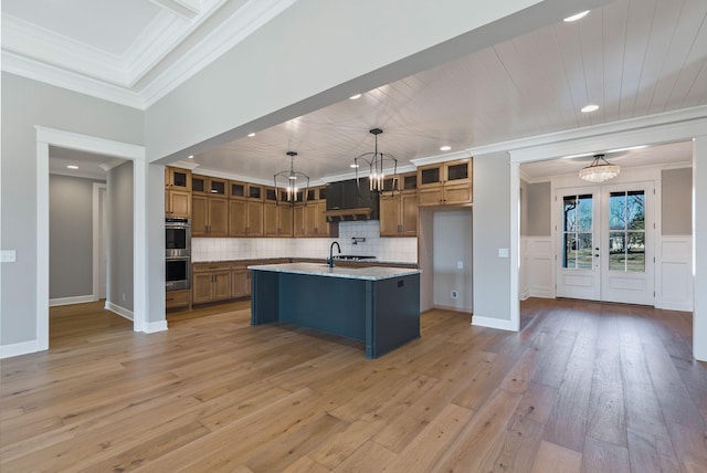 kitchen with a center island with sink, pendant lighting, light stone counters, and an inviting chandelier