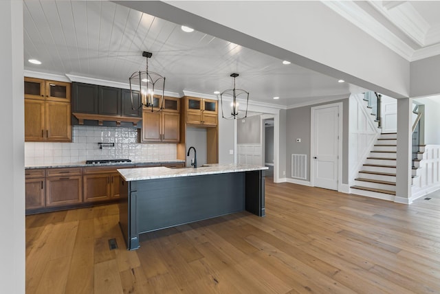 kitchen featuring pendant lighting, crown molding, gas cooktop, light stone countertops, and an island with sink