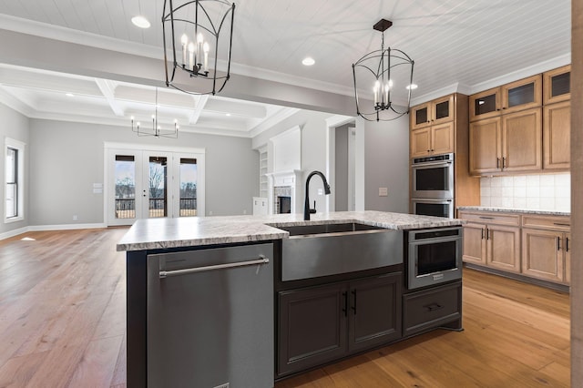 kitchen with appliances with stainless steel finishes, pendant lighting, decorative backsplash, a kitchen island with sink, and light hardwood / wood-style floors