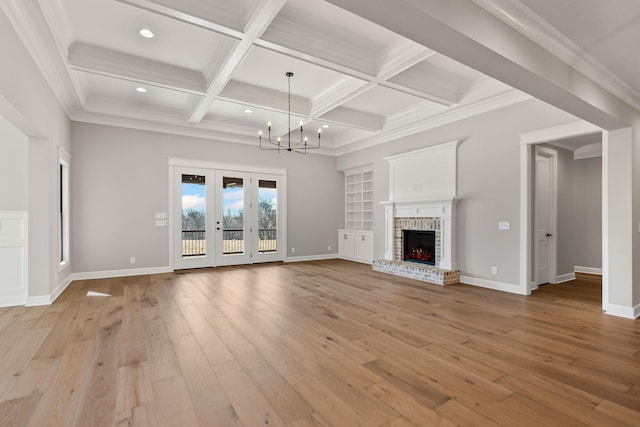 unfurnished living room featuring an inviting chandelier, beam ceiling, coffered ceiling, a brick fireplace, and light wood-type flooring