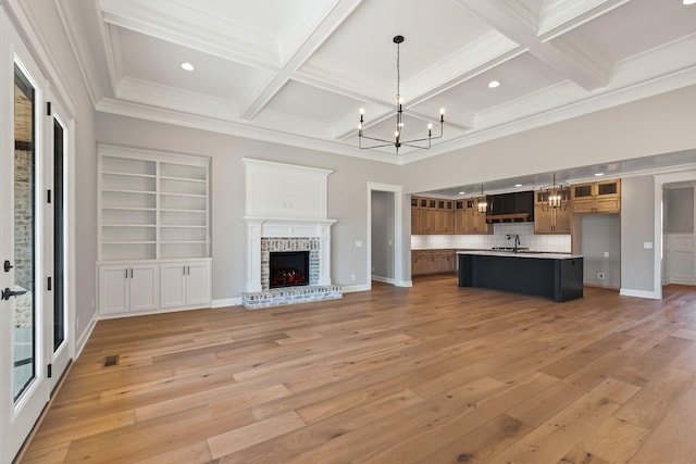 unfurnished living room with beamed ceiling, coffered ceiling, a fireplace, and a chandelier