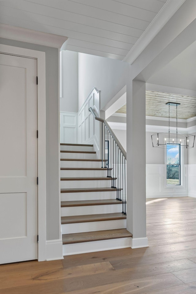 staircase with hardwood / wood-style flooring, ornamental molding, and a chandelier