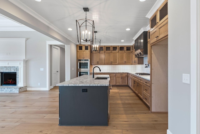 kitchen with sink, light stone counters, tasteful backsplash, pendant lighting, and a kitchen island with sink