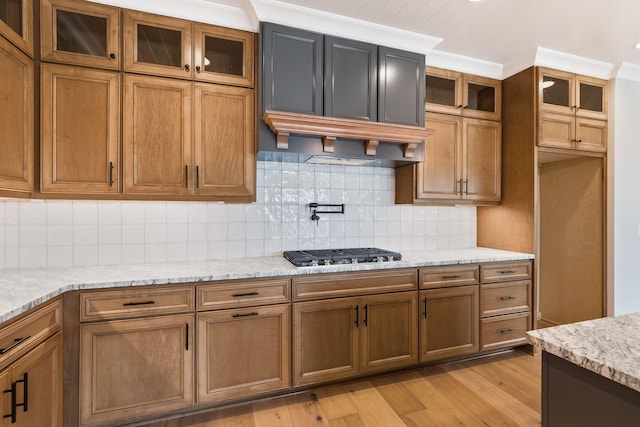 kitchen featuring light hardwood / wood-style flooring, light stone counters, ornamental molding, decorative backsplash, and stainless steel gas stovetop