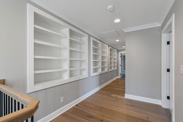 hall with built in shelves, ornamental molding, and wood-type flooring