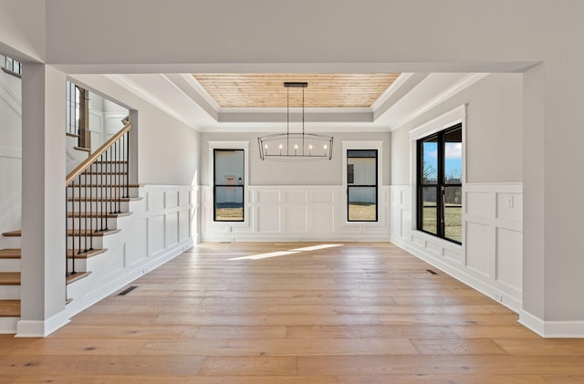 foyer entrance with ornamental molding, a tray ceiling, a chandelier, and light wood-type flooring