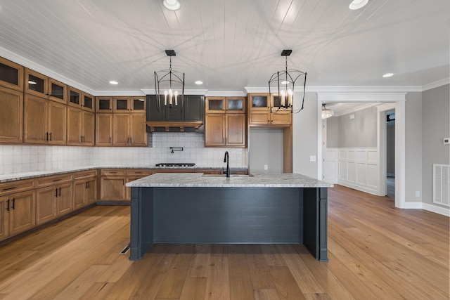 kitchen with ornamental molding, sink, hanging light fixtures, and a center island with sink