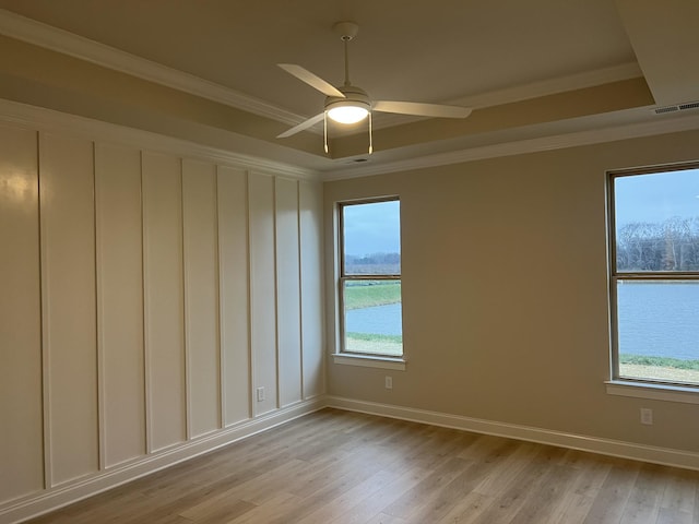 empty room with ceiling fan, light hardwood / wood-style floors, crown molding, and a tray ceiling