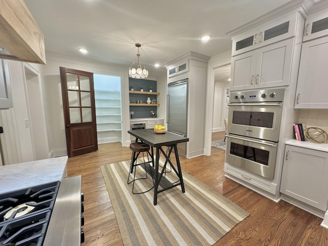 kitchen with hanging light fixtures, white cabinetry, light hardwood / wood-style flooring, and stainless steel appliances